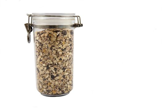 A transparent jar full of oats, fruits and nuts.