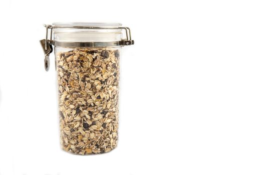 A transparent jar full of oats, fruits and nuts.