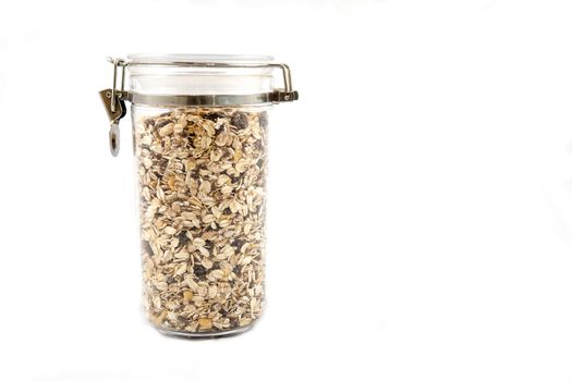 A transparent jar full of oats, fruits and nuts.