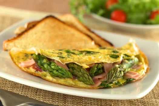 Green asparagus and ham omelet with toast bread and a fresh salad in the back (Selective Focus, Focus on the three asparagus tips in the front)