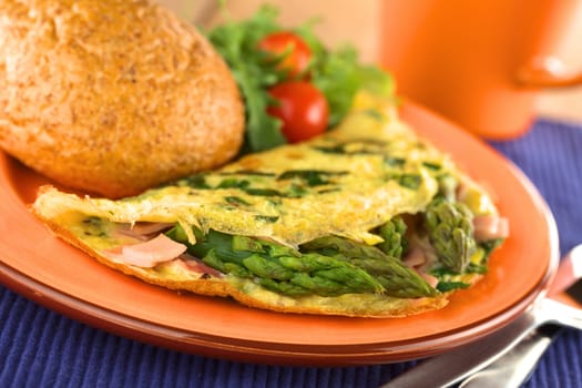 Green asparagus and ham omelet with wholewheat bun and salad on the plate and a mug in the back (Selective Focus, Focus on the asparagus head in the front)