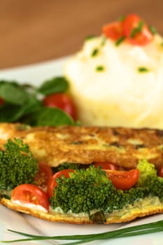 Broccoli and tomato omelette with mashed potato and watercress salad (Selective Focus, Focus on the broccoli floret in the front)