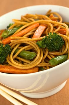 Vegetable and wholewheat spaghetti stir fry in white bowl with chopsticks (Selective Focus, Focus on the broccoli floret on the right)