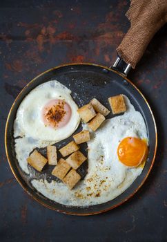 Frying pan full of scramble eggs from two eggs with a small pieces of toasted bread. Stands on grunge metal background.