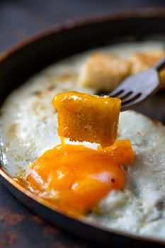 Frying pan full of scramble eggs from two eggs with a small pieces of toasted bread. Stands on grunge metal background.