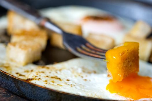 Frying pan full of scramble eggs from two eggs with a small pieces of toasted bread. Stands on grunge metal background.