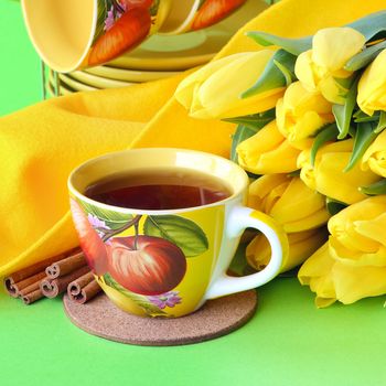 Tea cups and yellow tulips on green background