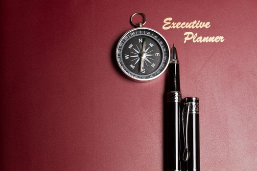 a dark red executive planner with a simple compass and two pens