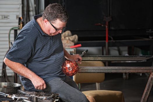 Glass craftsman holding rod with glass object cooling