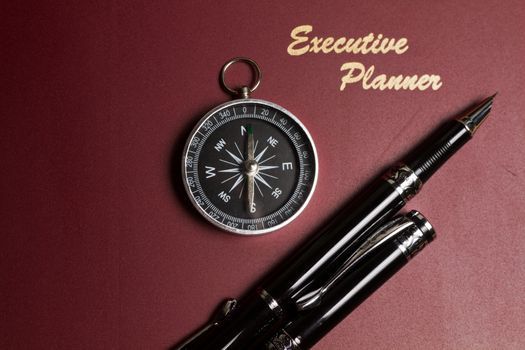 a dark red executive planner with a simple compass and two pens in landscape orientation