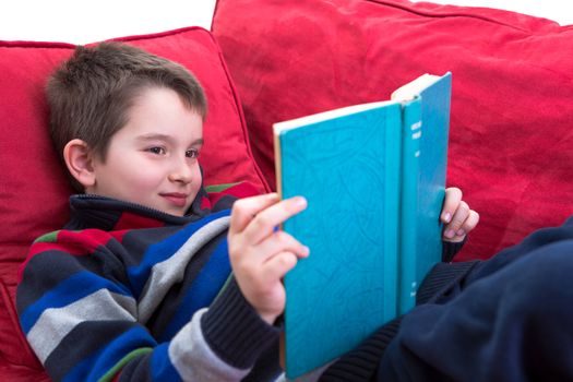 Kid enjoy reading the novel on the comfortable red couch.