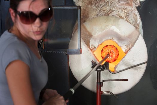 Young female glass artist putting object in hot kiln