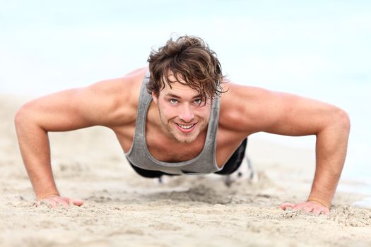 fitness man exercising push ups smiling happy. Male fitness model cross-training on beach. Caucasian man in his twenties.
