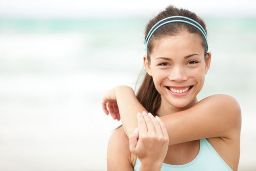 Fitness woman exercising smiling happy stretching out doing workout on beach. Beautiful mixed race Asian Caucasian female fitness model portrait.