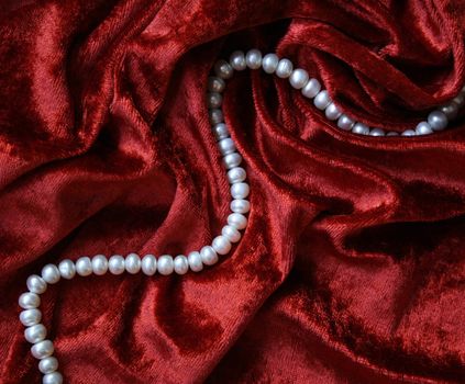 Necklace of white pearls on a terracotta velvet as background 