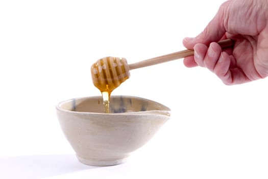 Man's hand holding a dripping honey dipper over a bowl.