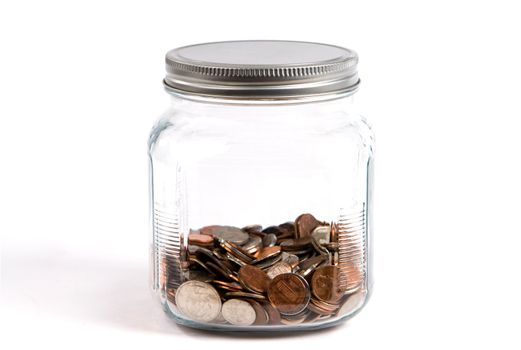 Spare change jar or piggybank holds coins in a glass container on white background.