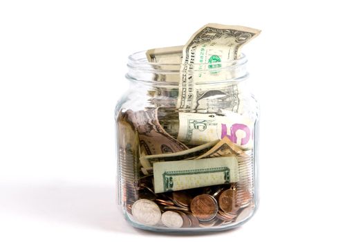 US dollars and coins fill a glass tip jar with money.