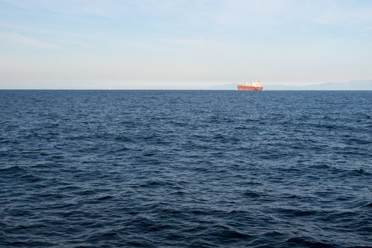 Small red cargo ship in very large ocean