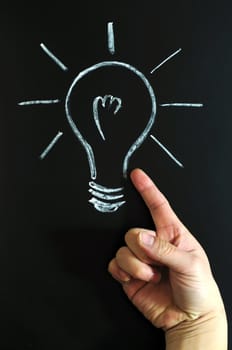 Light bulb drawn with chalk on blackboard, with a finger pointing to it