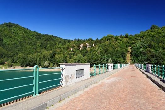 smal pave road across Brugneto lake dam on a sunny day, Liguria, Italy