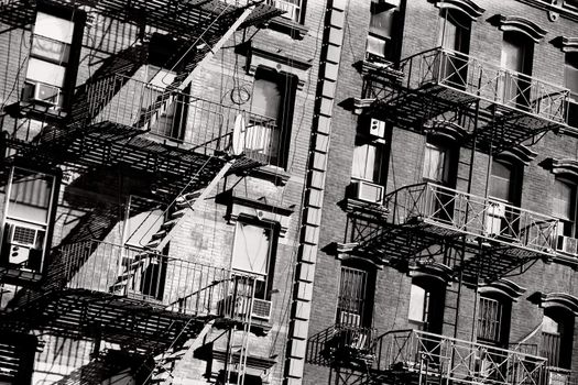 Black and white photo of the exterior of a building in New York with old fire escape.
