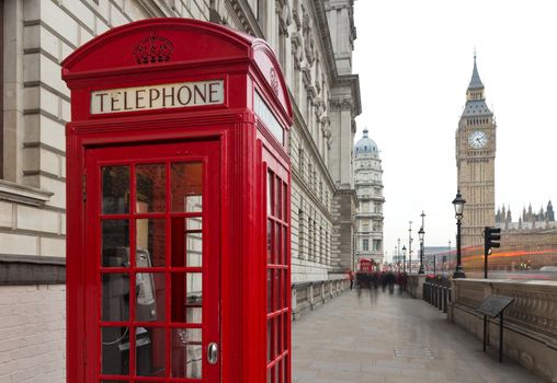 Traditional red telephone box in London public phone - a symbol of the city. Fragment of booths with the Big Ben in the background of the evening