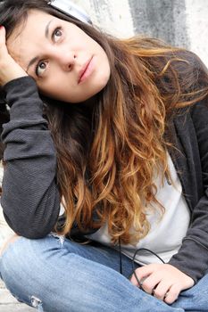 A young woman listening to melancholic Music and sitting on the pavement.