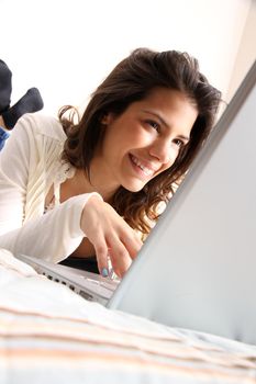 A young girl laying on the bed and surfing on the Internet with a Laptop.  
