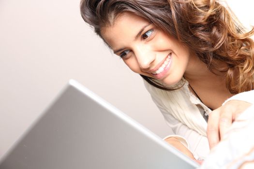 A young girl laying on the bed and surfing on the Internet with a Laptop.  
