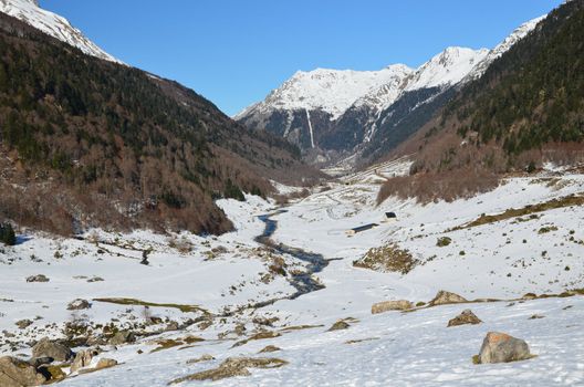 Winter Lanscape of Osseu valley (vallee d'Ossau) close to Col de Portalet,  mountain pass at Spanish border, Atlantic Pyrenees, Aquitaine, Bearn, France. River Le gave d'Ossau, Farmers refuge and animal houses are in the down, snowy Pic de la Sagette is at background
