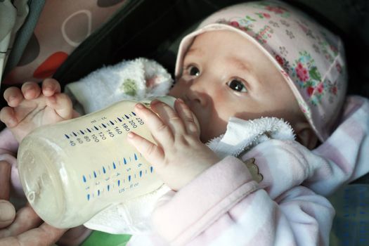 The little girl eats porridge from a bottle