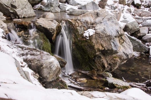 Slow flowing creek in the snow and rocks.