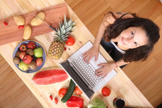 A young woman using a Laptop while cooking.