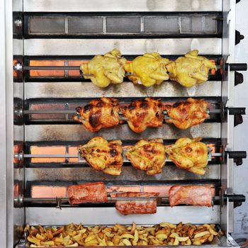 Whole chickens and pork on rotisserie spit and patatoes in a market