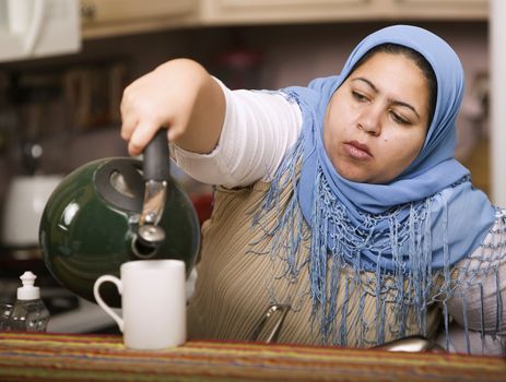 Muslim woman wearing a head scarf in a western kitchen pouring tea