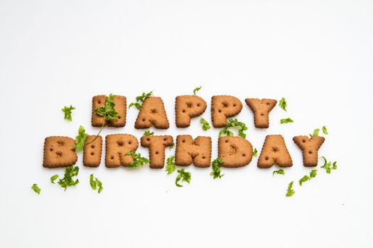 the words Happy Birthday made by brown biscuits and green leaves on white surface in landscape orientation