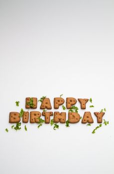 the words Happy Birthday made by brown biscuits and green leaves on white surface in portrait orientation