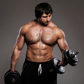 Muscular guy working out with dumbbells over grey background