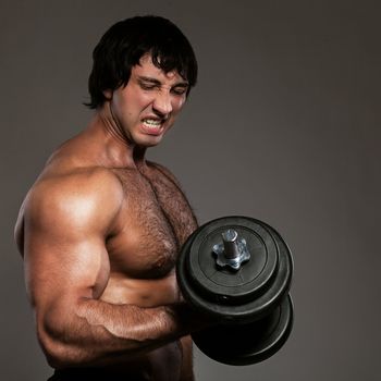 Muscular guy working out with dumbbells over grey background