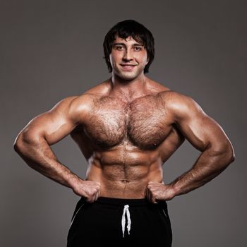 Muscular guy working out with dumbbells over grey background