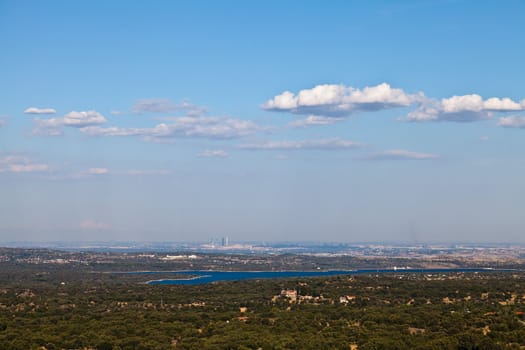 View of the city of Madrid from a distance. Bright blue lake in the foreground. Taken on a sunny day with bright blue sky and a few white clouds.