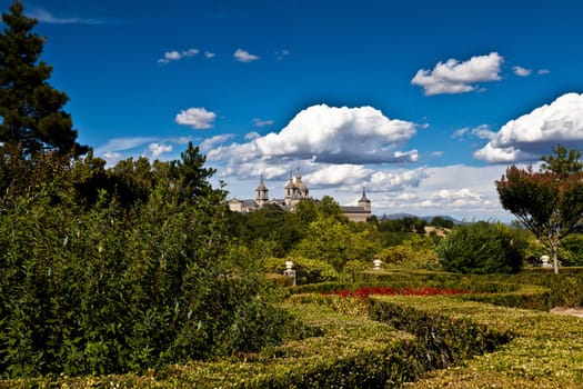 San Lorenzo de El Escorial Monastery from Casita del Infante. The towers of the church and monastery are set of by a bright blue sky.