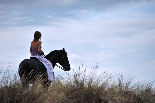 young woman and her black stallion in a field
