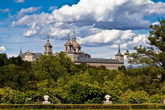 San Lorenzo de El Escorial Monastery from Casita del Infante. The towers of the church and monastery are set of by a bright blue sky.