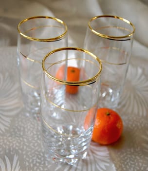 Three glasses, decorated with gold spiral pattern, and two tangerines