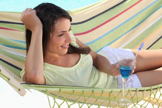 Woman drinking cocktail whilst lying on hammock