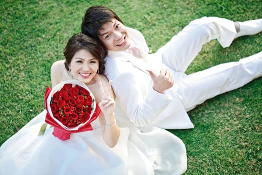 portrait of bride and groom sitting on fresh grass with rose bouquet