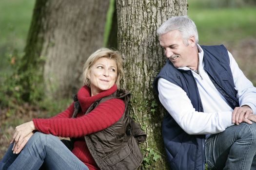 Middle-aged couple sat by tree