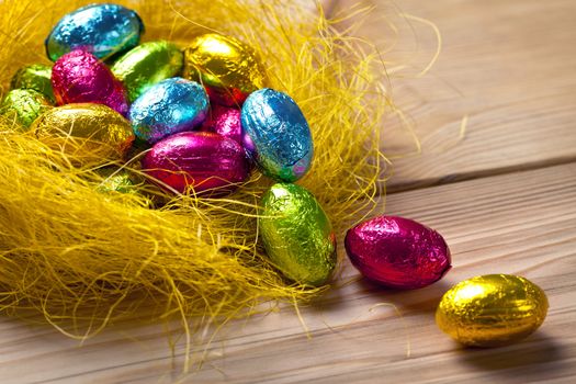 Chocolate easter eggs in yellow nest on wooden table background. Holiday composition